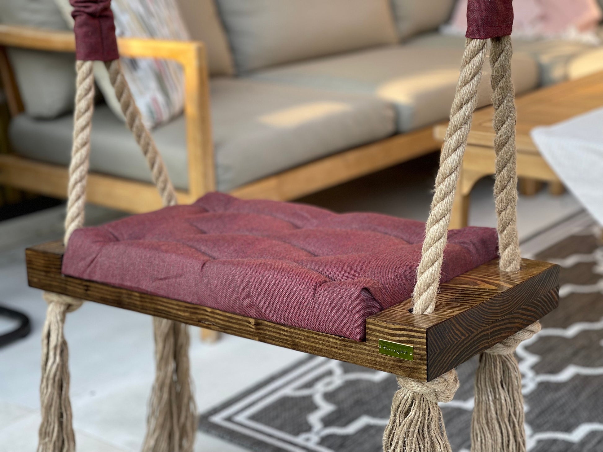 Outdoor wooden swing with burgundy quilted cushion